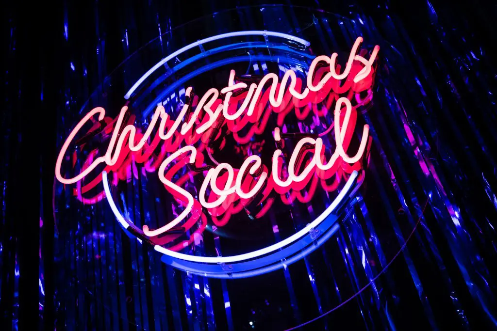 Neon Christmas Social sign against a blue tinsel backdrop
