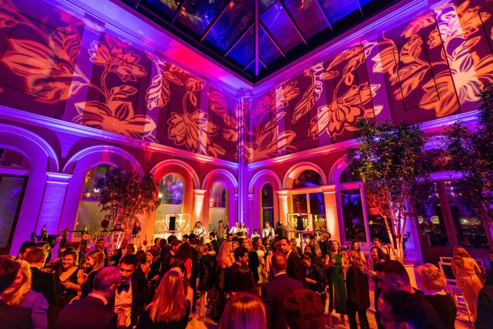 Guests filling an ornate hall lit in pink and purple
