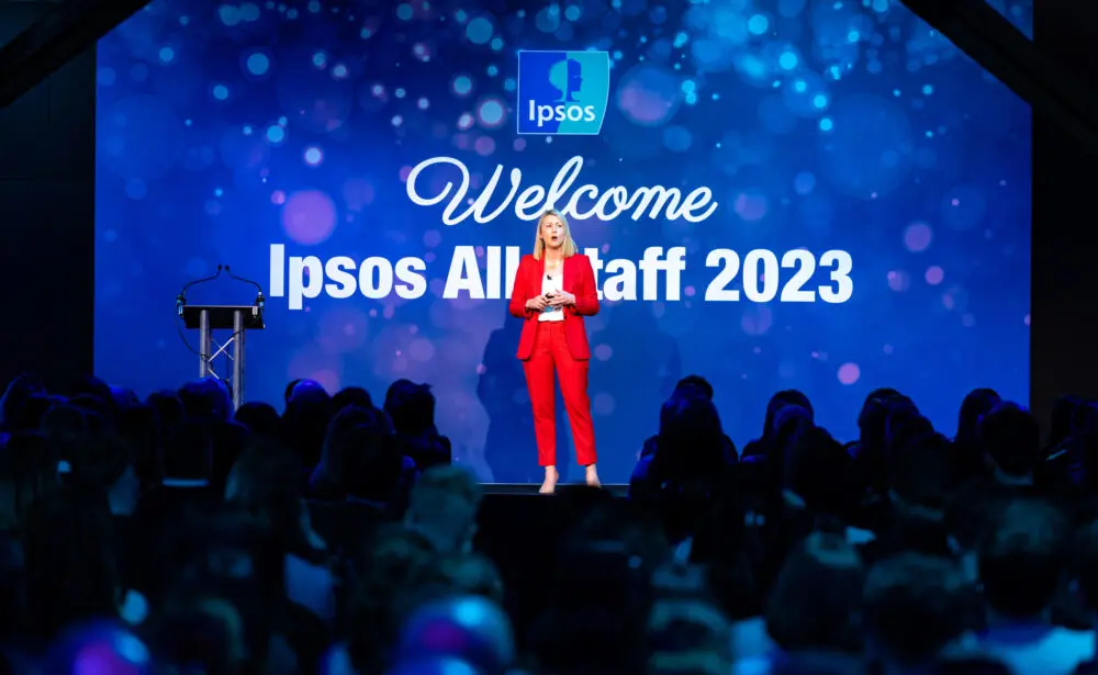 Host on stage in front of a welcome screen at the Ipsos all-staff conference