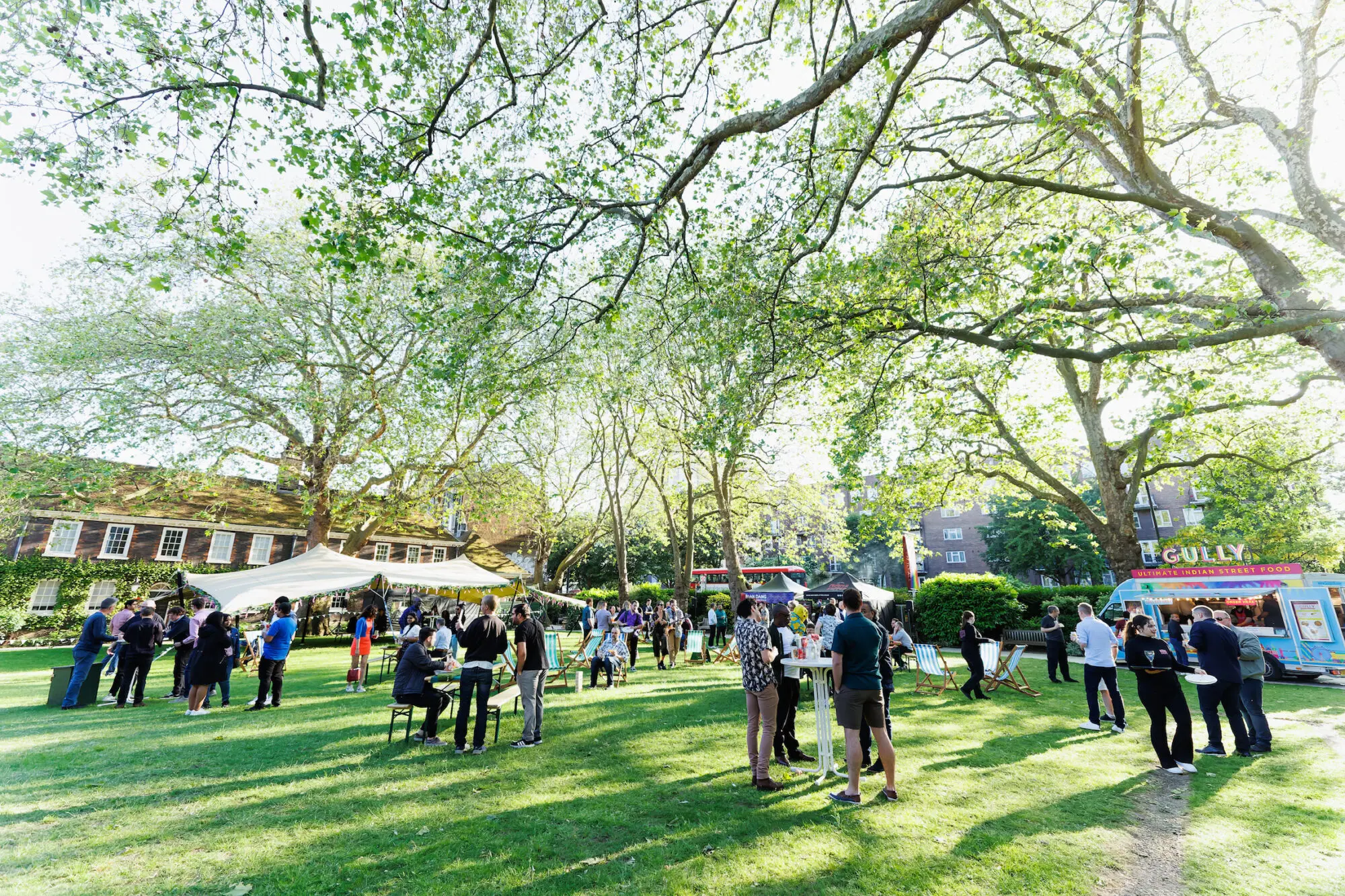 Guests at an outdoor summer event beneath mature trees