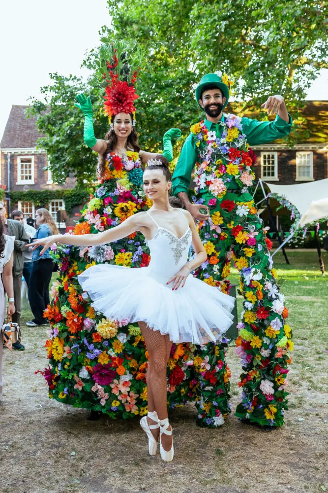 Flower-costumed stilt walkers and a ballerina performing at a garden party